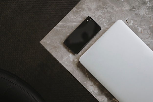 Ordenador portátil y un teléfono en una mesa de mármol.