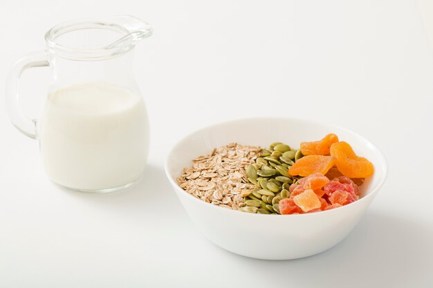 Ordeñe con el tazón de fuente sano de muesli, las semillas de calabaza y las frutas secas en el tazón de fuente blanco en el fondo blanco