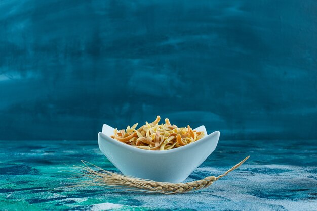 Oreja de trigo y un plato de fideos caseros, sobre el fondo azul.