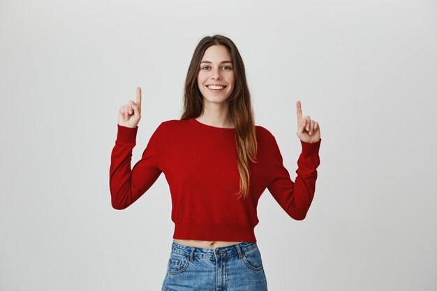 Orgullosa, feliz niña sonriente apuntando los dedos hacia arriba en promo