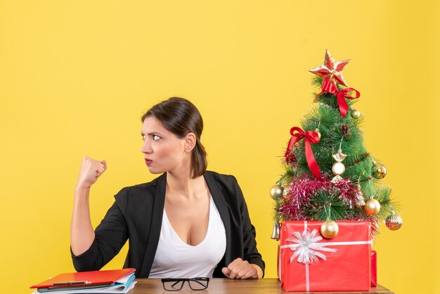 Orgullosa joven en traje con árbol de Navidad decorado en la oficina en amarillo