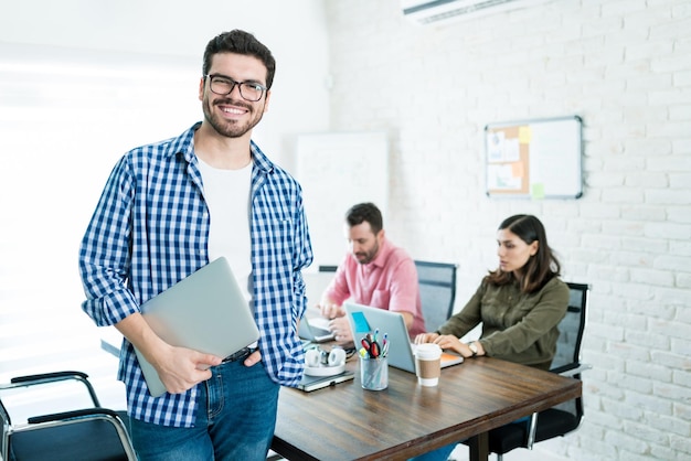 Foto gratuita orgulloso empresario sosteniendo portátil mientras está de pie con compañeros de trabajo en segundo plano.