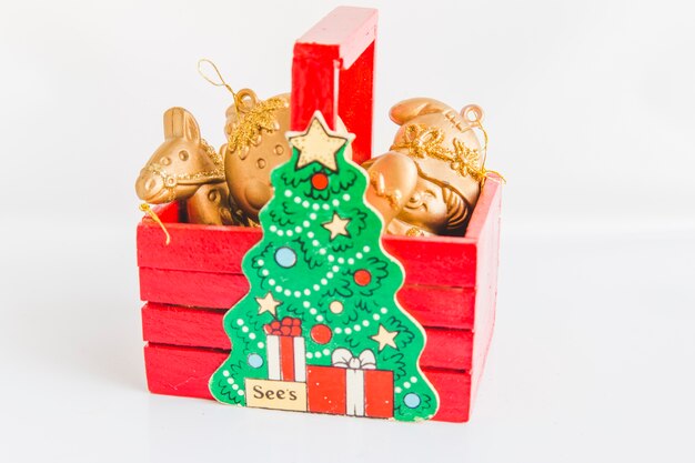 Ornamentos de oro de la Navidad en la caja de madera roja con el árbol de navidad en el fondo blanco