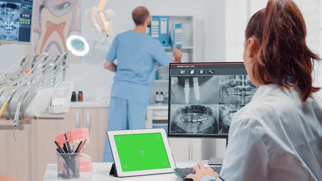 Ortodoncista con pantalla verde horizontal en tableta para cuidado bucal y odontología. Mujer que trabaja como dentista con clave de croma y plantilla de maqueta aislada mientras mira escaneo de dientes