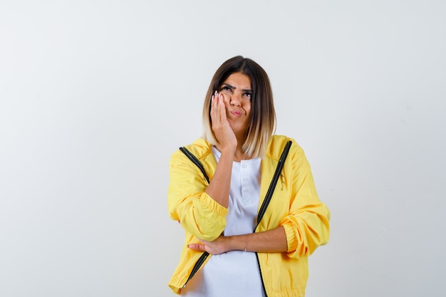 Ortrait de dama manteniendo la mano en la mejilla en camiseta, chaqueta y mirando pensativo vista frontal