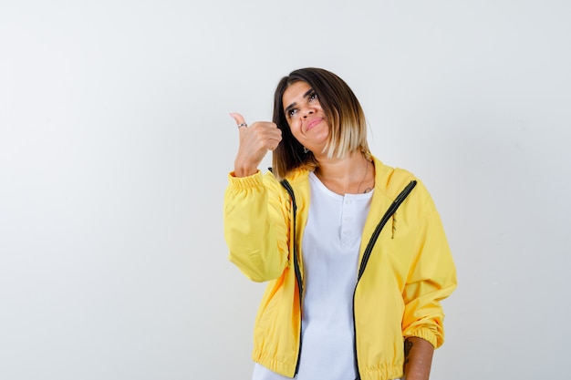 Ortrait de dama mostrando el pulgar hacia arriba en camiseta, chaqueta y mirando alegre vista frontal