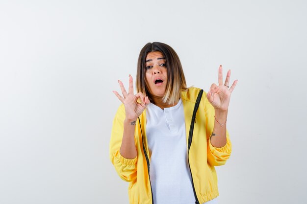 Ortrait de mujer mostrando gesto ok en camiseta, chaqueta y mirando asombrado vista frontal