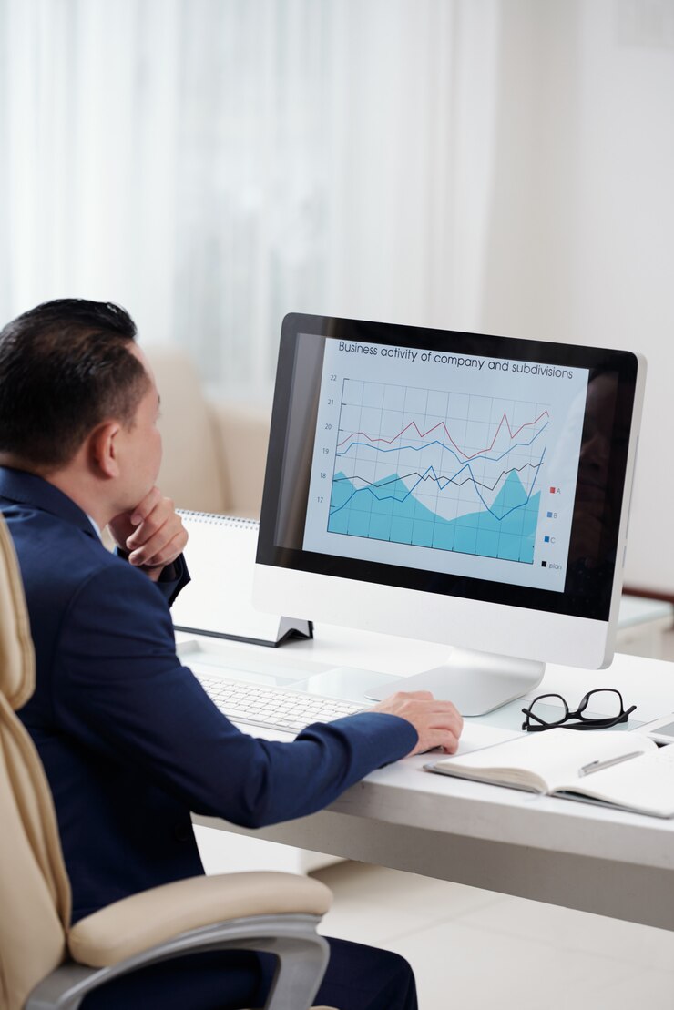 Photo Gratis over the shoulder view of entrepreneur analysing the business graph on the screen of his desktop computer