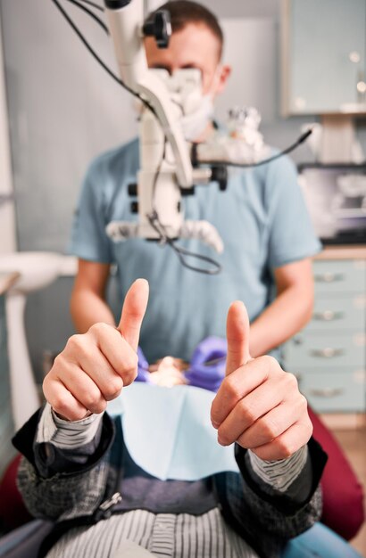 Paciente femenina dando pulgares hacia arriba durante el procedimiento dental