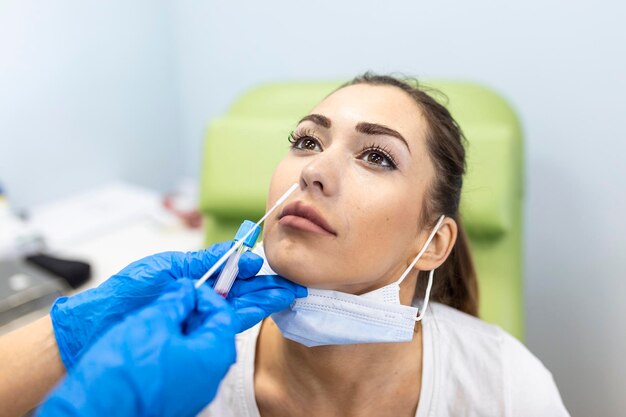 Paciente femenina a la que se le realiza la prueba de Covid19 con un hisopo nasal por parte de un profesional de la salud protegida con guantes y traje de PPE Prueba rápida de antígeno durante la pandemia del coronavirus