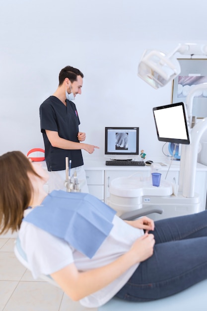 Paciente femenino que miente en la silla del dentista que mira rayos X de los dientes en la pantalla