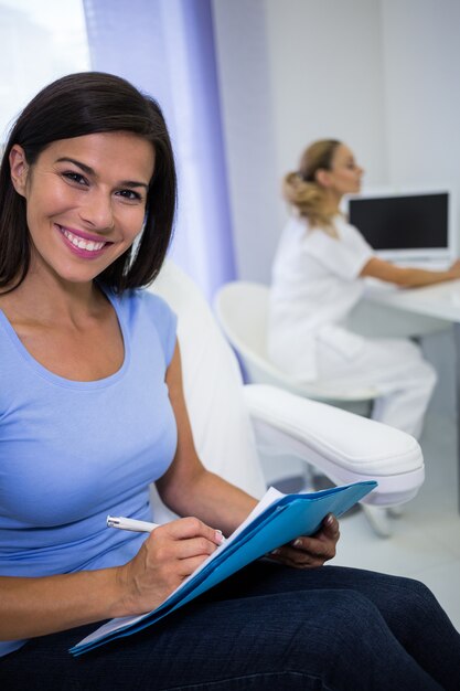 Paciente femenino sonriente escribiendo en un expediente médico