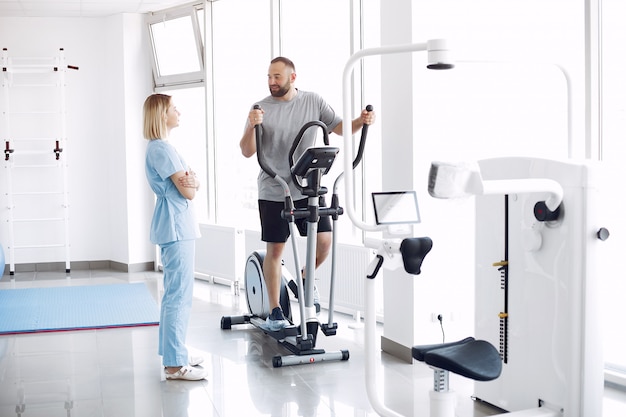 Paciente haciendo ejercicio en bicicleta de spinning en el gimnasio con el terapeuta