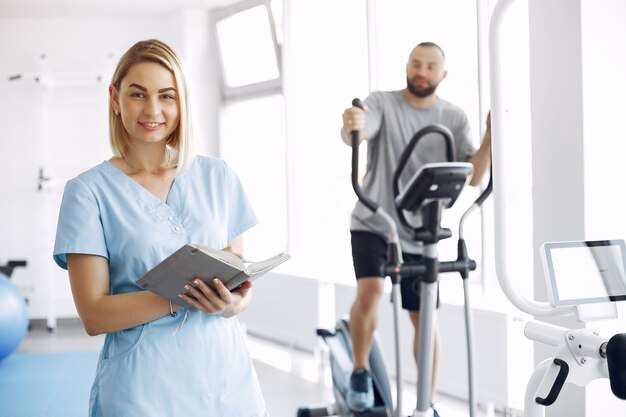 Paciente haciendo ejercicio en bicicleta de spinning en el gimnasio con el terapeuta