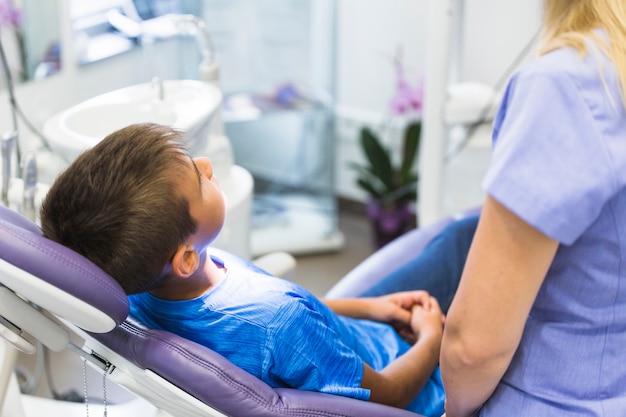 Foto gratuita paciente infantil apoyado en silla dental en clínica