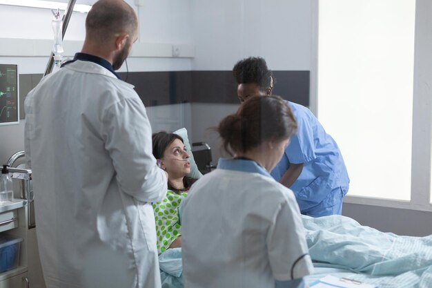 El paciente ingresado en el hospital recuperándose en la cama recibiendo atención médica profesional de una enfermera experimentada mientras los médicos examinan los síntomas. Equipo de médicos que consultan la enfermedad de la mujer durante las rondas.