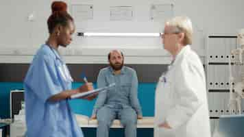 Foto gratuita paciente joven sentado en el gabinete médico y esperando los resultados del examen para conocer el diagnóstico de la enfermedad. persona enferma que asiste a la cita de consulta con el equipo de personal médico en la oficina.