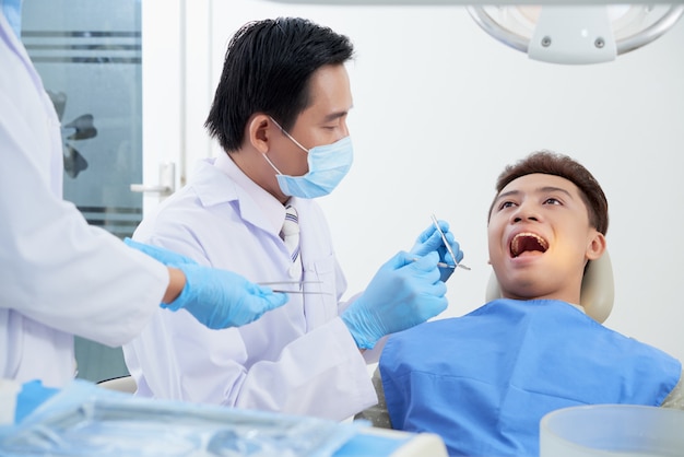 Paciente masculino asiático recostado con la boca abierta y el dentista examinando sus dientes