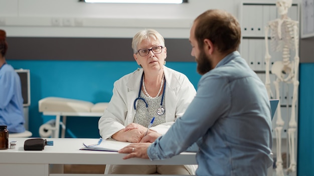 Foto gratuita paciente masculino que firma el informe de la cita de control en los documentos para recibir tratamiento y medicamentos recetados. firma en documentos de diagnóstico médico para apoyo al sistema de salud en oficina.