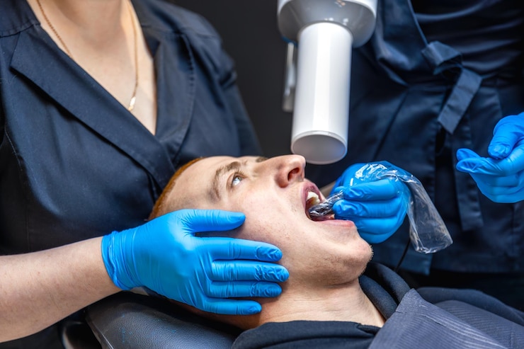 Foto gratuito paciente masculino tendido en una silla en el consultorio dental tratamiento dental dentista comprobando los dientes