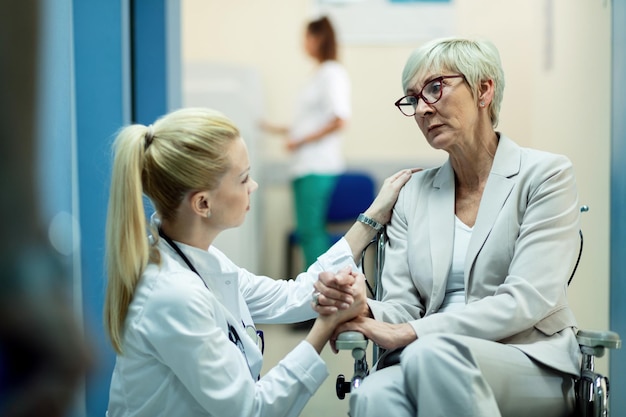 Una paciente mayor en silla de ruedas se siente preocupada mientras se comunica con una doctora y se toma de la mano