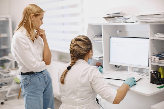 Foto gratuita paciente mujer en el consultorio médico. doctor en máscara médica. el doctor usa la computadora.