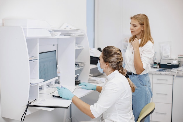 Foto gratuita paciente mujer en el consultorio médico. doctor en máscara médica. el doctor usa la computadora.