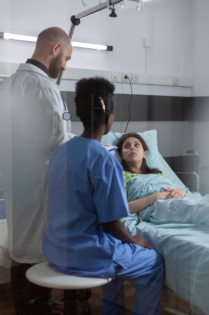 Paciente mujer enferma descansando en la cama hablando con el médico explicando los síntomas de la enfermedad mientras escribe ...