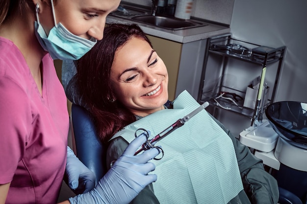 Paciente mujer sentada en una silla de dentista mientras su médico se prepara para la inyección de jeringa.