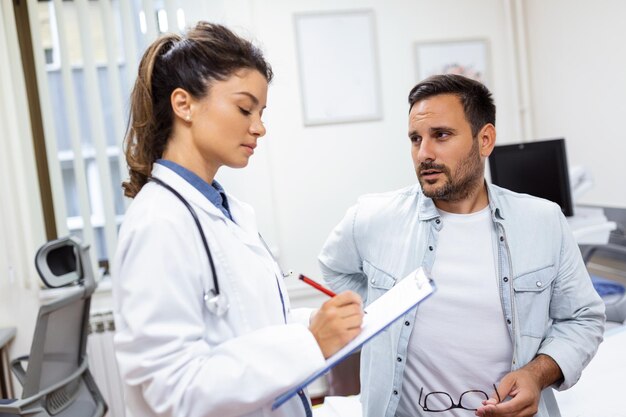 Paciente que le cuenta al médico sobre su dolor y problemas de salud durante la visita al hospital Joven que se queja de dolor de espalda o riñón mientras está sentado en la cama de examen en el consultorio del médico