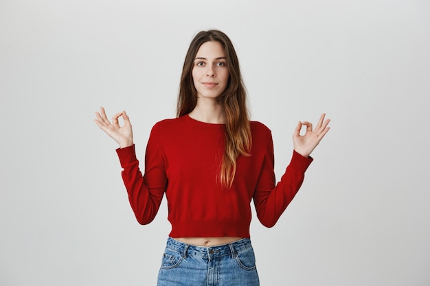 Paciente y relajada, sonriente joven mujer bonita meditando, tomarse de las manos en el gesto mudra