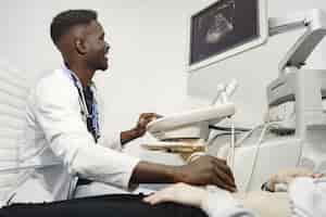 Foto gratuita paciente en el sofá. el médico hace un diagnóstico por ultrasonido. hombre con uniforme blanco.