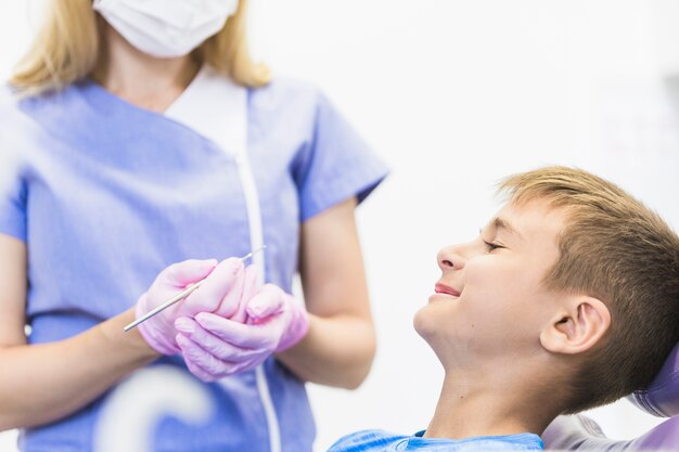 Paciente sonriente del niño delante del dentista de sexo femenino que sostiene el escalador