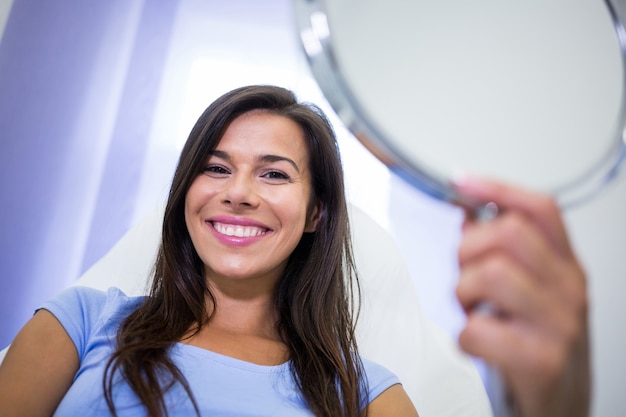 Paciente sonriente que sostiene un espejo en la clínica