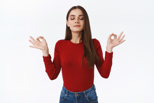 Paciente y tranquila joven afroamericana de mentalidad sana con suéter rojo respira cogidos de la mano de lado con el signo de la paz zen cierra los ojos e inhala aire fresco mientras se relaja durante la meditación