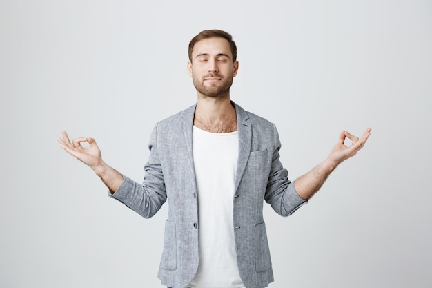 Paciente y tranquilo chico barbudo meditando con los ojos cerrados