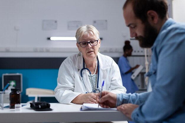 Paciente en visita médica firmando archivos de chequeo para médico y cita. Especialista en atención médica que solicita la firma de documentos para el hombre, dando tratamiento contra el diagnóstico en el consultorio.