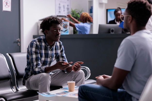 Pacientes afroamericanos esperando en el vestíbulo para asistir a un examen médico, hablando sobre el apoyo de atención médica antes de la cita. Adultos con enfermedad a la espera de recibir medicamentos y tratamiento.