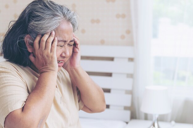 Pacientes de edad avanzada en la cama, pacientes asiáticos mayores con dolor de cabeza manos en la frente - concepto médico y sanitario