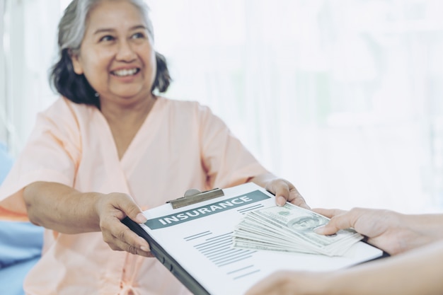 Pacientes de edad avanzada mujer lesionada en la cama del paciente en el hospital con billetes de un dólar estadounidense se siente feliz de obtener dinero del seguro de las compañías de seguros