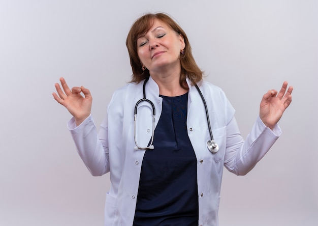 Pacífica doctora de mediana edad vistiendo bata médica y estetoscopio haciendo bien firmar en pared blanca aislada