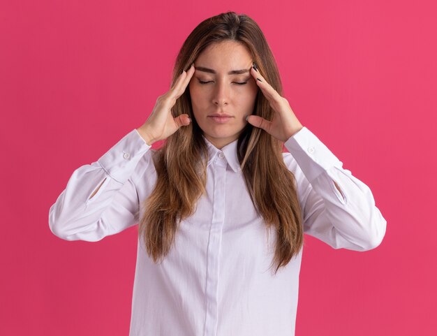 Pacífica joven bastante caucásica se encuentra con los ojos cerrados poniendo las manos en las sienes