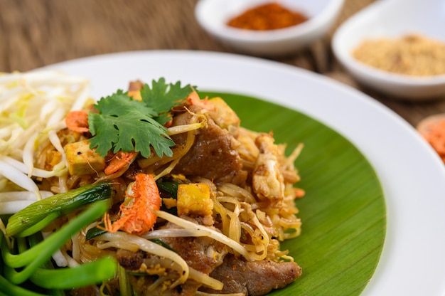 Pad Thai en un plato blanco con limón, huevos y condimentos en una mesa de madera.