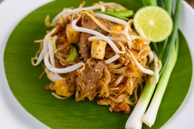 Foto gratuita pad thai en un plato blanco con limón sobre una mesa de madera