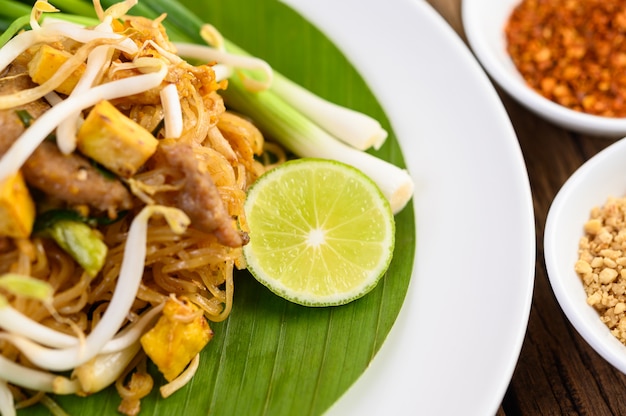 Pad Thai en un plato blanco con limón sobre una mesa de madera