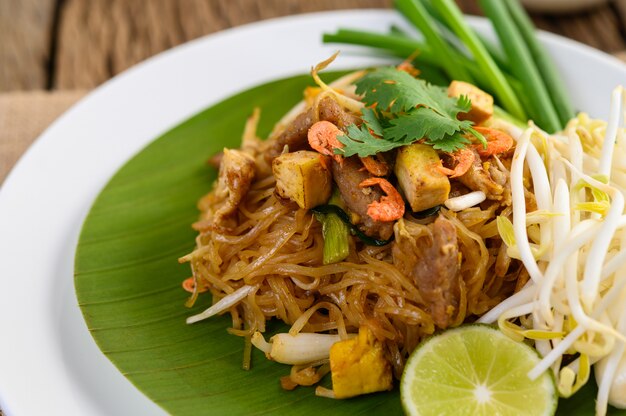 Pad Thai en un plato blanco con limón sobre una mesa de madera