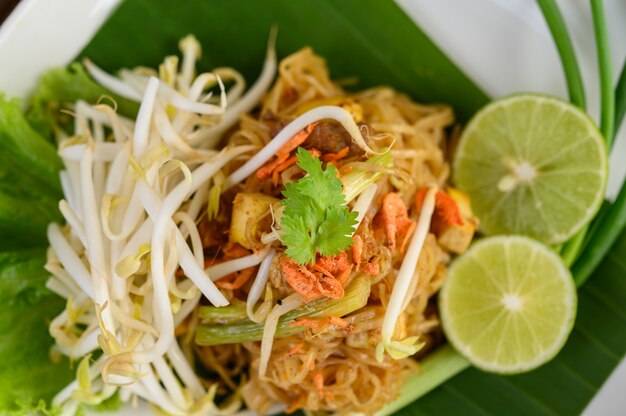 Pad Thai en un plato blanco con limón sobre una mesa de madera