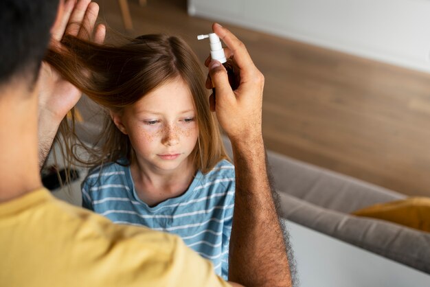 Padre de alto ángulo usando tratamiento para piojos para niña