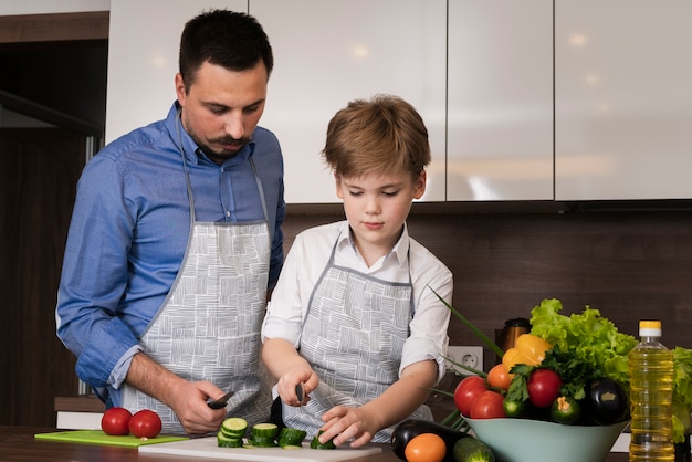 Foto gratuita padre de ángulo bajo enseñando a hijo a cortar verduras