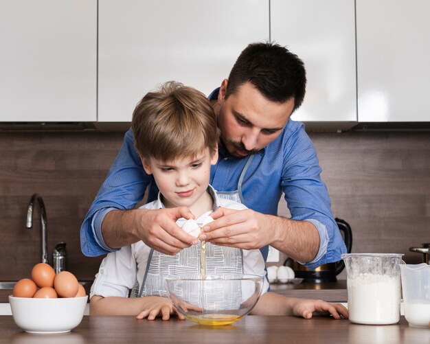 Padre de ángulo bajo enseñando a hijo a romper huevos